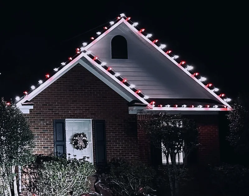 Lit Christmas wreath and roofline detail on a brick home
