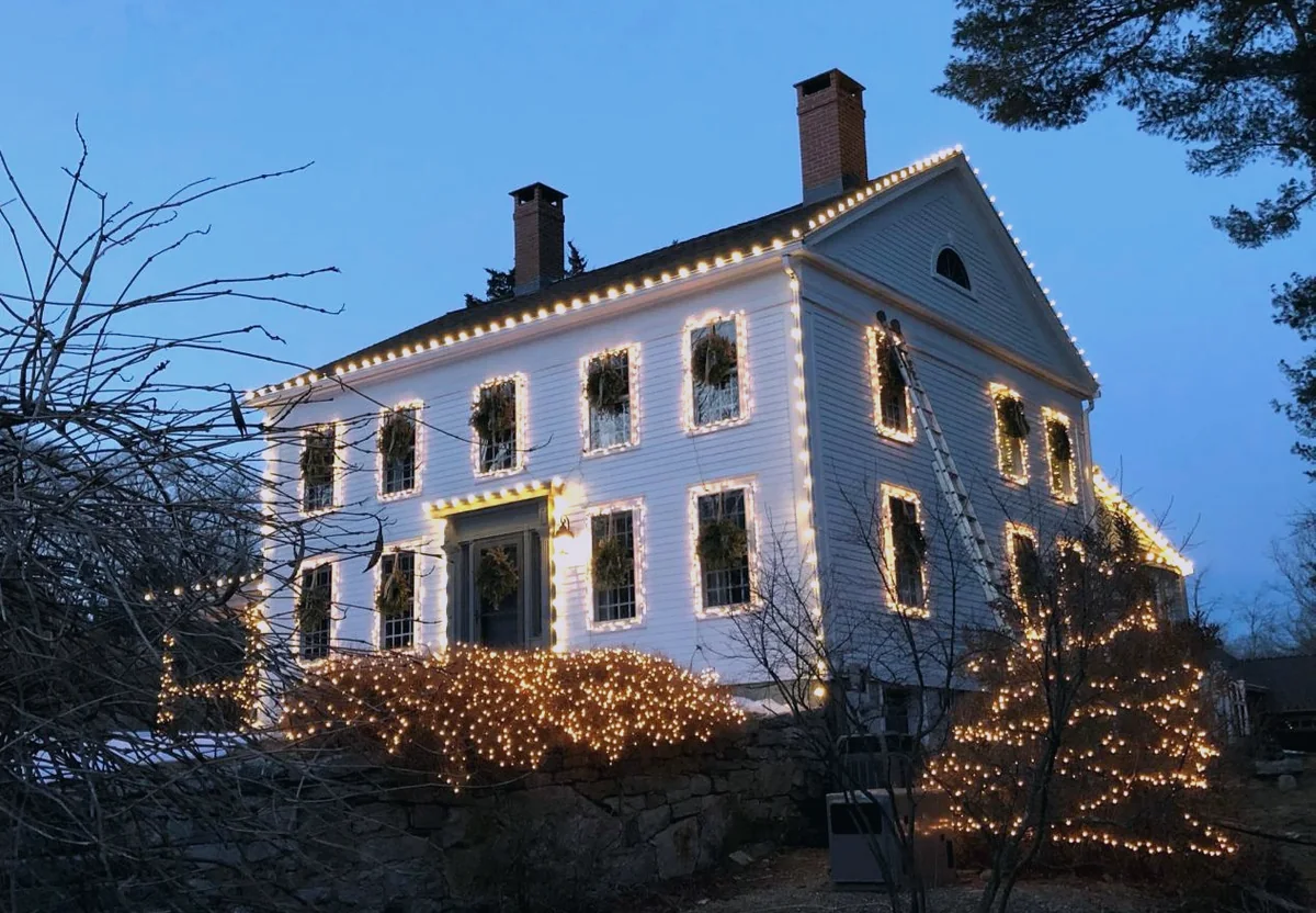 White colonial outlined in warm white with every window framed and shrubs lit