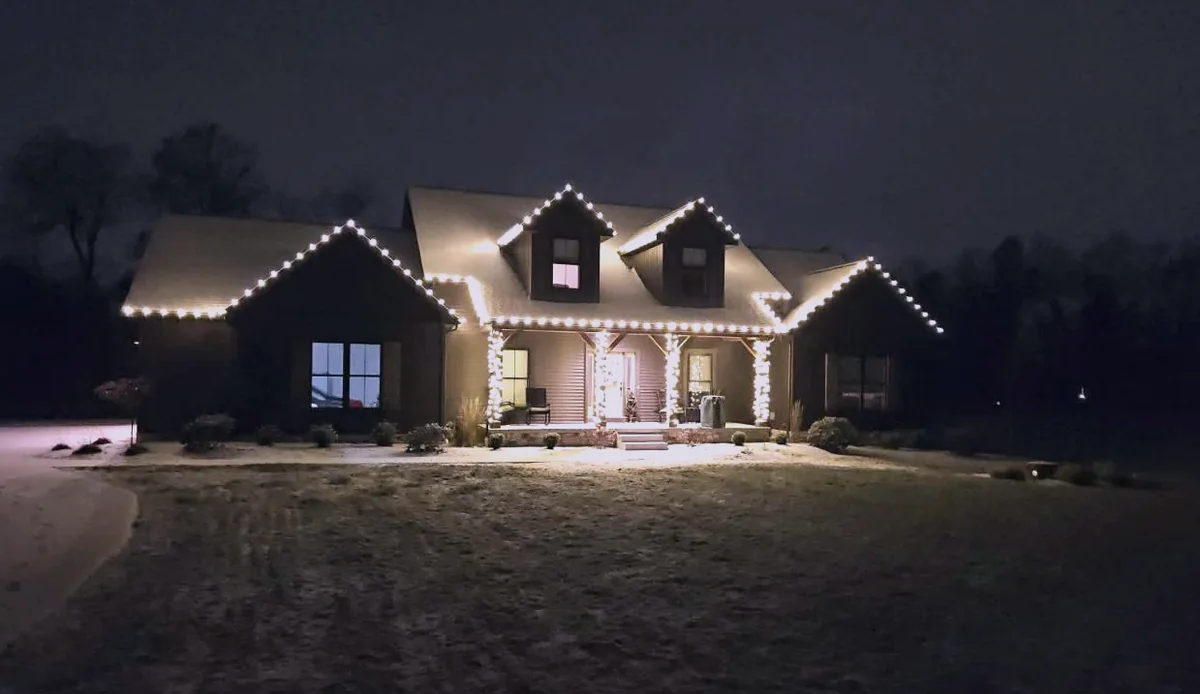 Farmhouse with dormers outlined in warm white including wrapped porch posts