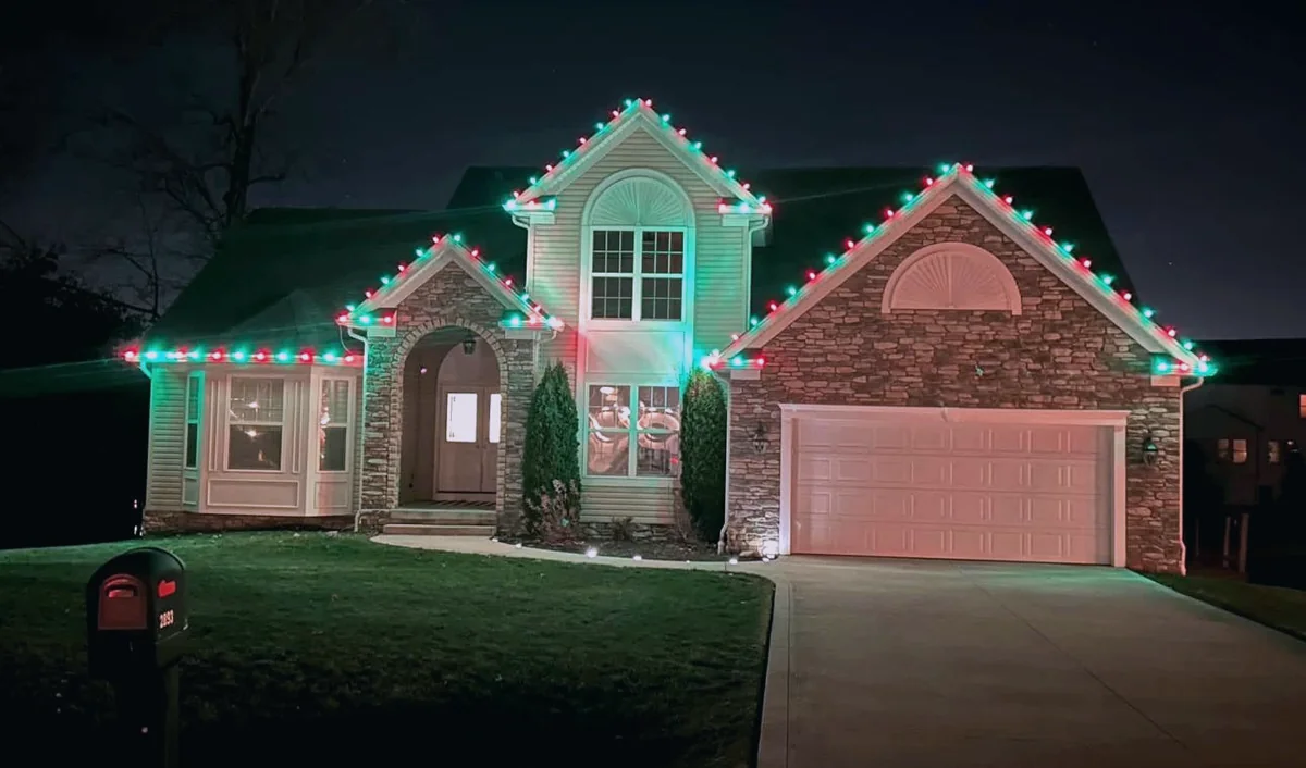 Red and green C9 bulbs along the roofline of a multi-gable stone and siding home