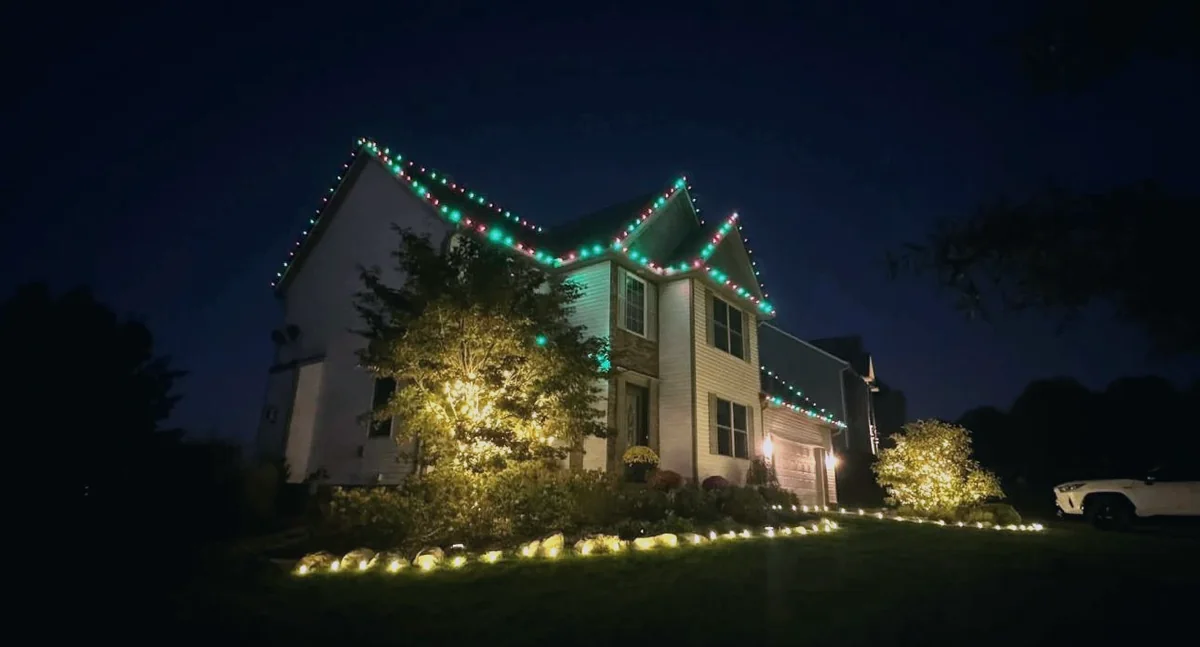 Red and green roofline at dusk with uplit trees and a lit walkway border