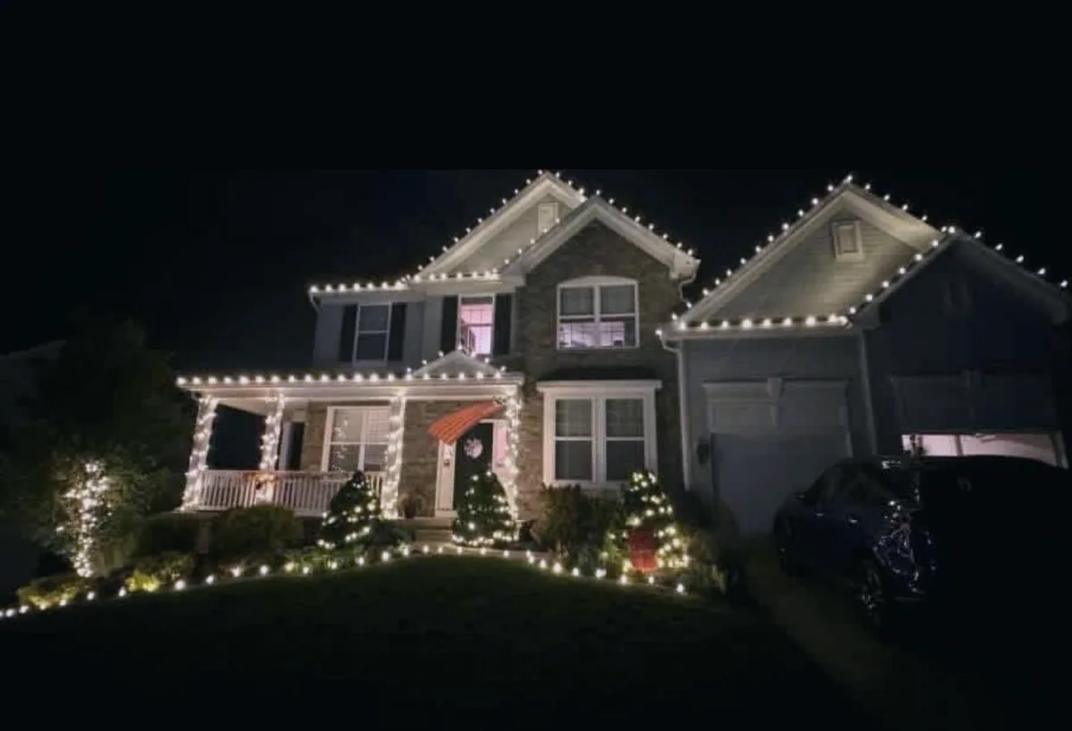 Two-story home with warm white roofline, wrapped porch columns and lit shrubs